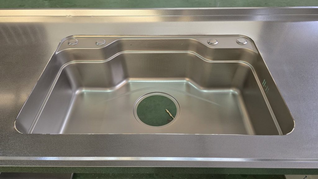 Góc chậu rửa bo tròn tinh tế, liền khối hoàn toàn với mặt bàn inox vân sần, xóa sổ hoàn toàn khe hở nấm mốc.